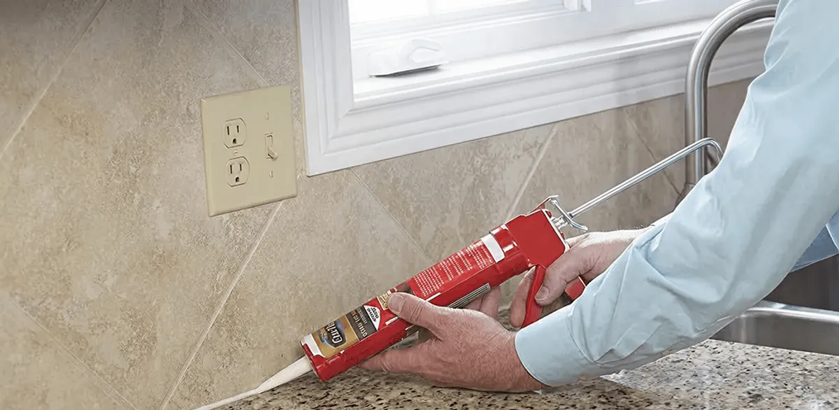 Handyman applying caulk along a kitchen backsplash and countertop seam in Santa Ana, CA
