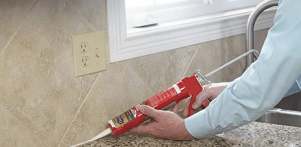 Handyman applying caulk along a kitchen backsplash and countertop seam in Santa Ana, CA