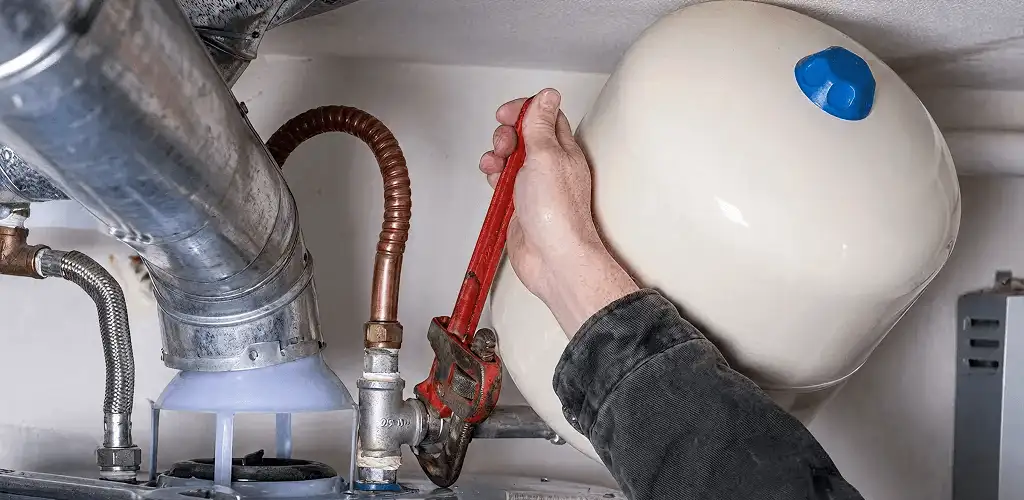 Water heater repair technician tightening plumbing connections near a tank unit in Santa Ana, CA